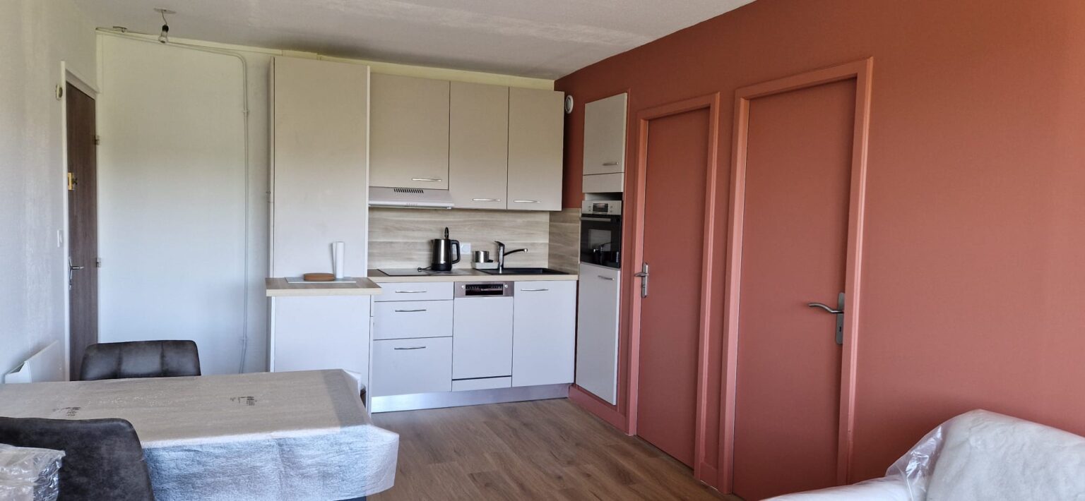 Cuisine moderne compacte avec placards blancs, mur rose et parquet stratifié