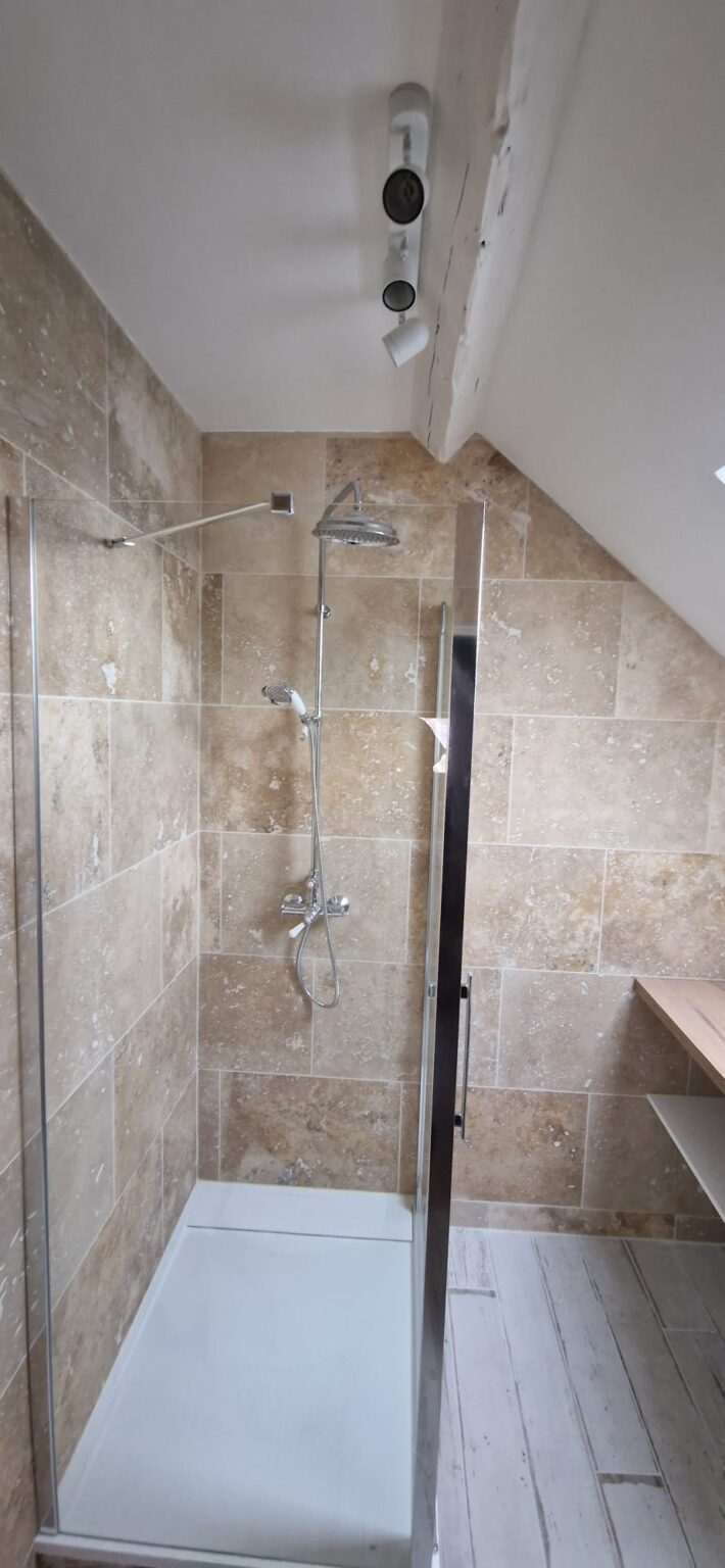 Douche italienne en carrelage pierre beige avec paroi verre et sol bois clair