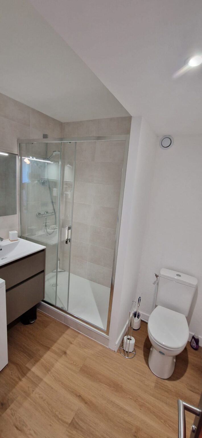 Salle de bain moderne avec douche vitrée, meuble vasque marron et toilettes
