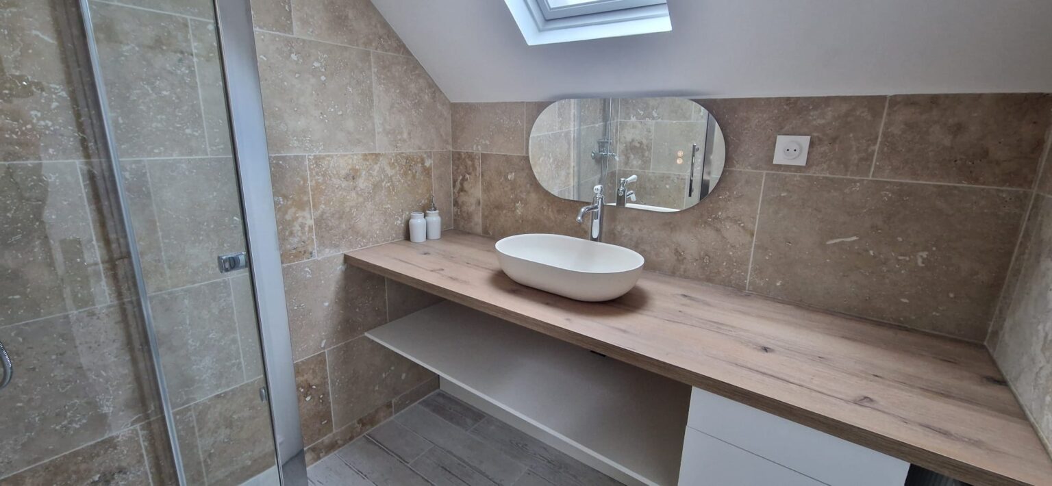 Salle de bain sous pente avec lavabo ovale, plan bois, miroir et carrelage beige