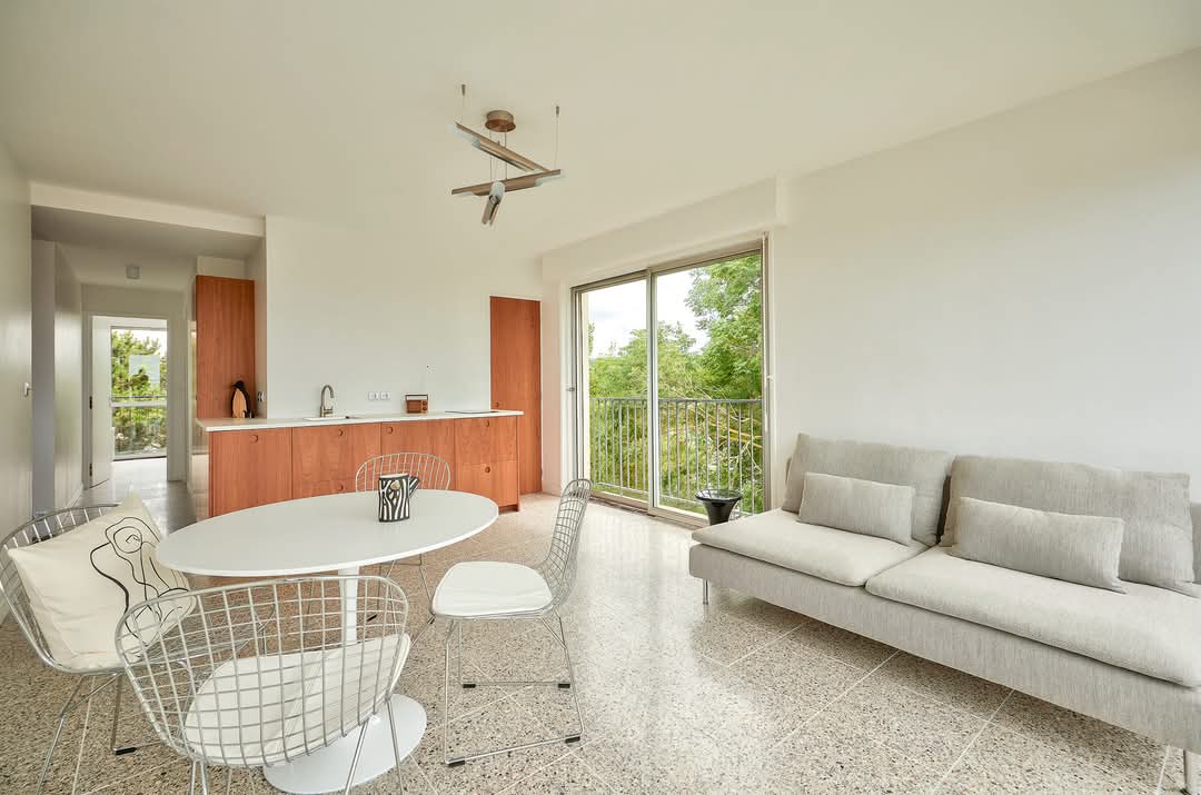 Salon moderne avec canapé gris et cuisine ouverte en bois clair sous baie vitrée
