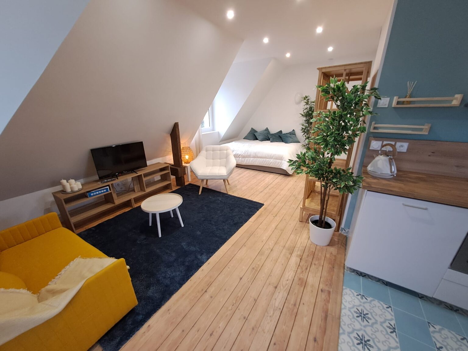 Studio aménagé avec canapé jaune, lit blanc et cuisine moderne