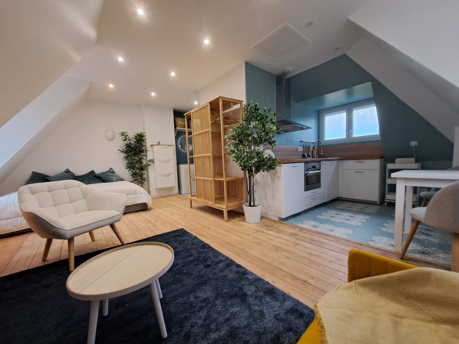 Studio sous combles avec cuisine blanche, parquet clair et mobilier moderne