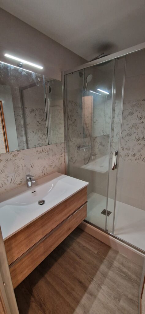 Salle de bain rénovée avec meuble sous-vasque bois, douche italienne paroi vitrée et carrelage décoratif